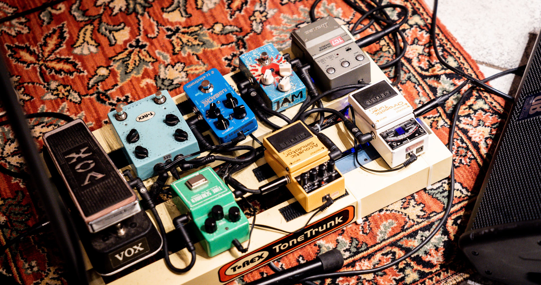 A guitar pedalboard on a patterned rug