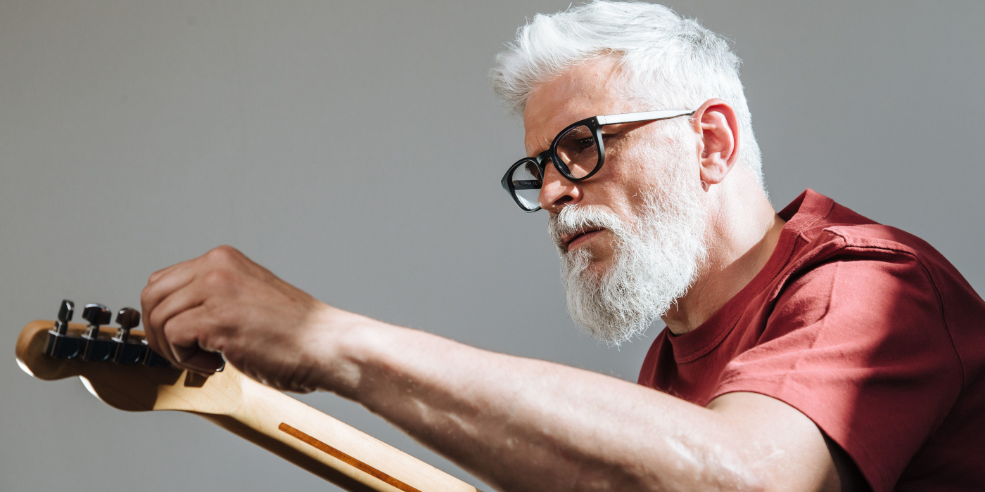 An older man tuning an electric guitar