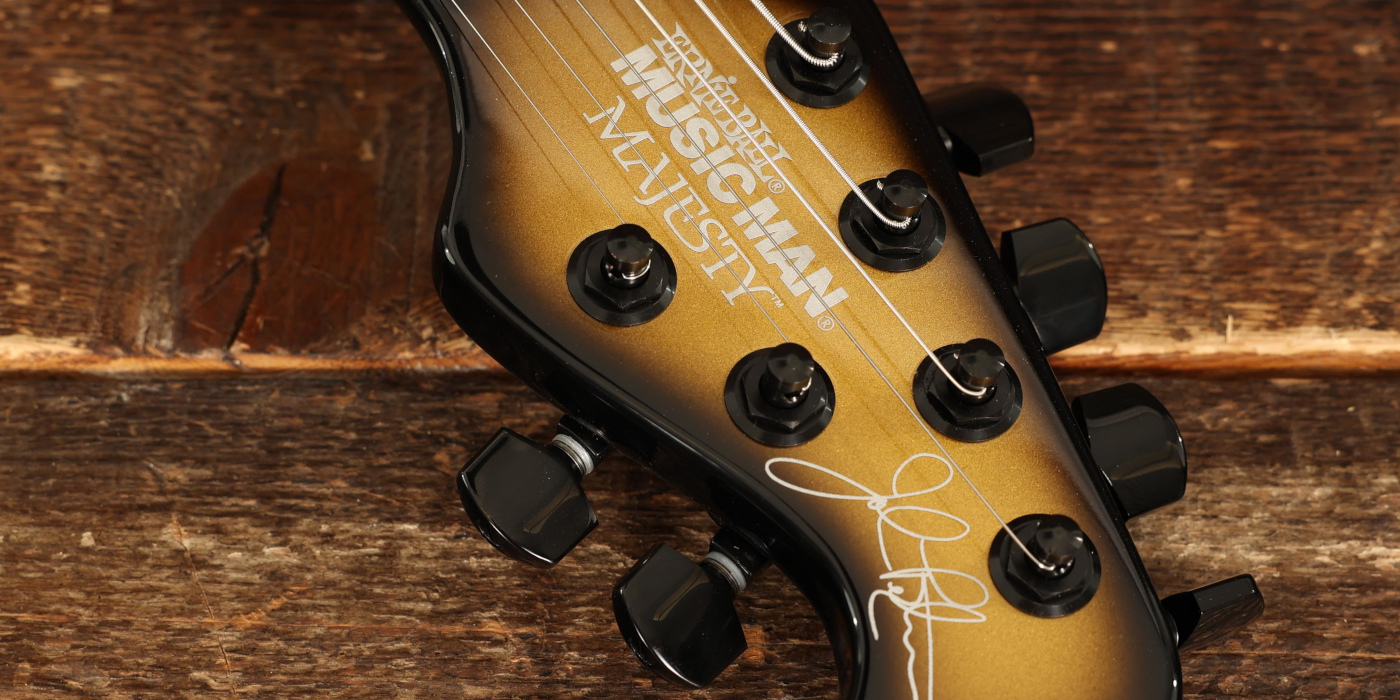 A photo of the front of a Music Man Majesty headstock against a wooden background