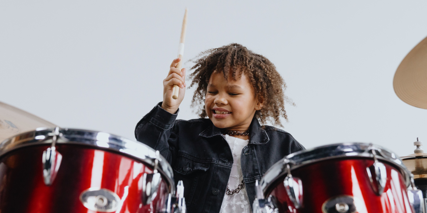 A young child playing a drum kit while holding a drumstick up in the air