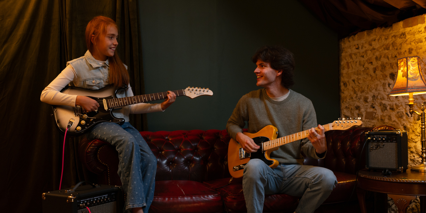 A boy and girl playing electric guitars while sitting on a sofa