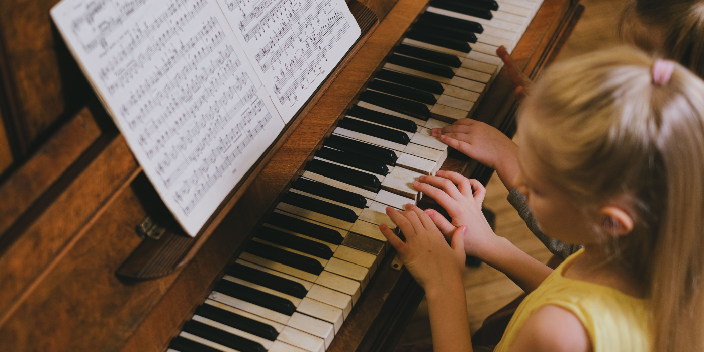 A young girl playing a piano while reading sheet music