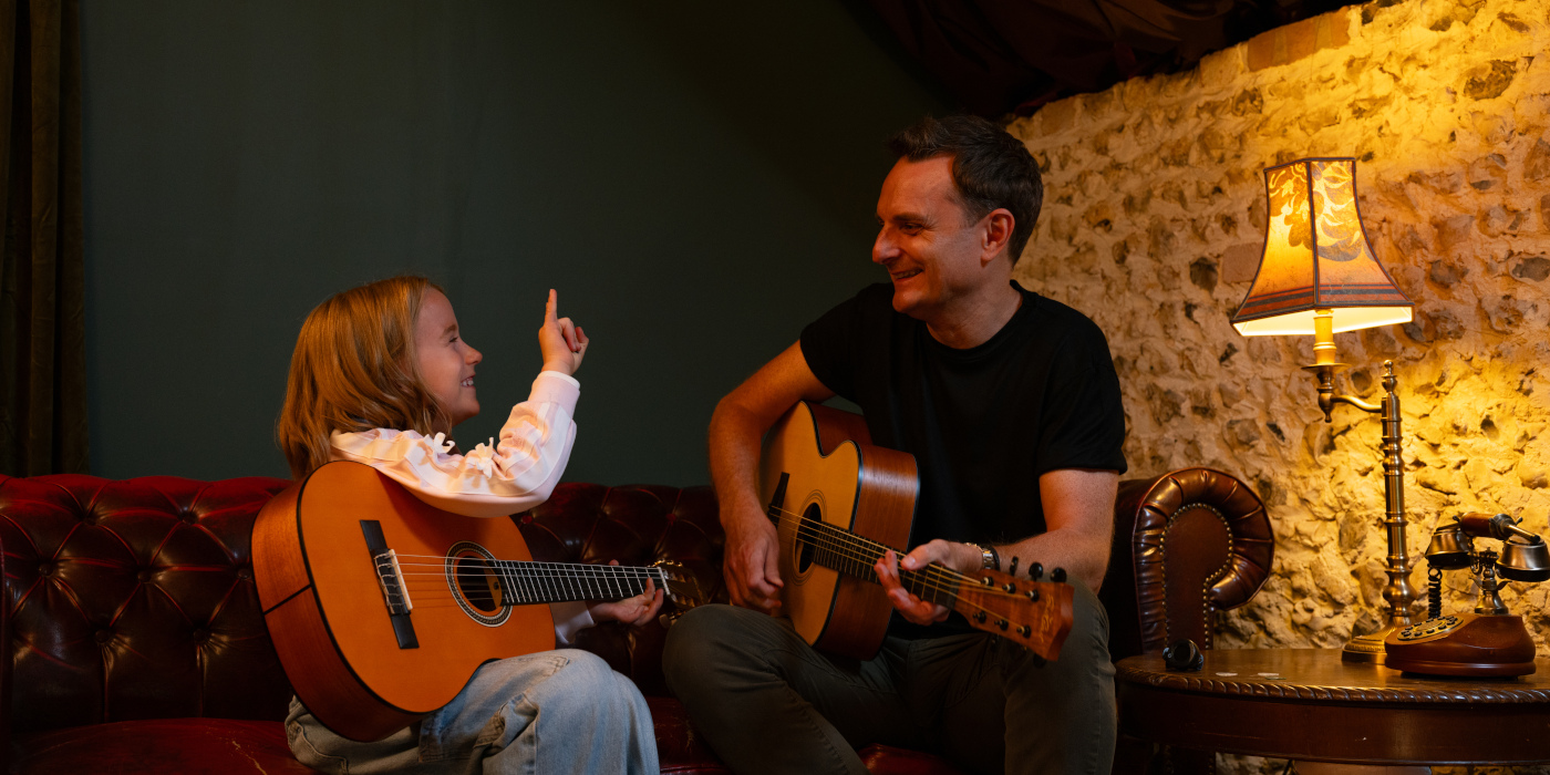Lee Anderton and a young child playing acoustic guitars on a sofa