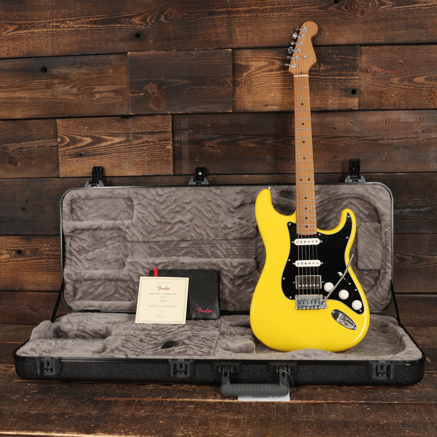 A Fender American Ultra II Strat HSS guitar in Graffiti Yellow in its included case against a wooden background
