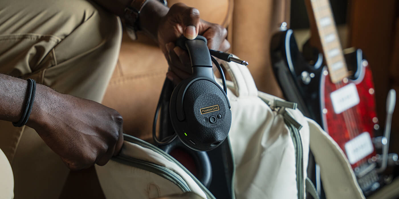Positive Grid Spark NEO Core guitar amp headphones being taken out of a backpack by a man with a guitar in the background