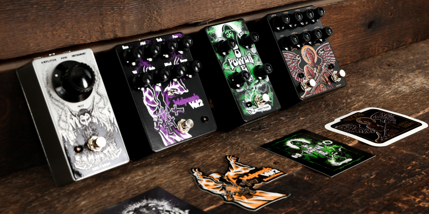 Four Does It Doom pedals lined up against a wooden background at an angle with stickers in front of them