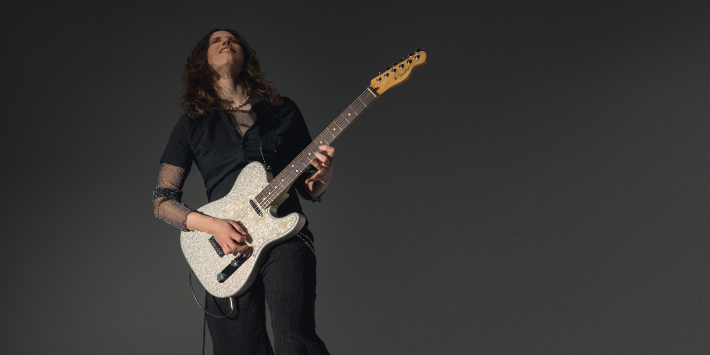 A female guitarist playing the Fender 75th Anniversary Player II Telecaster against a grey textured background