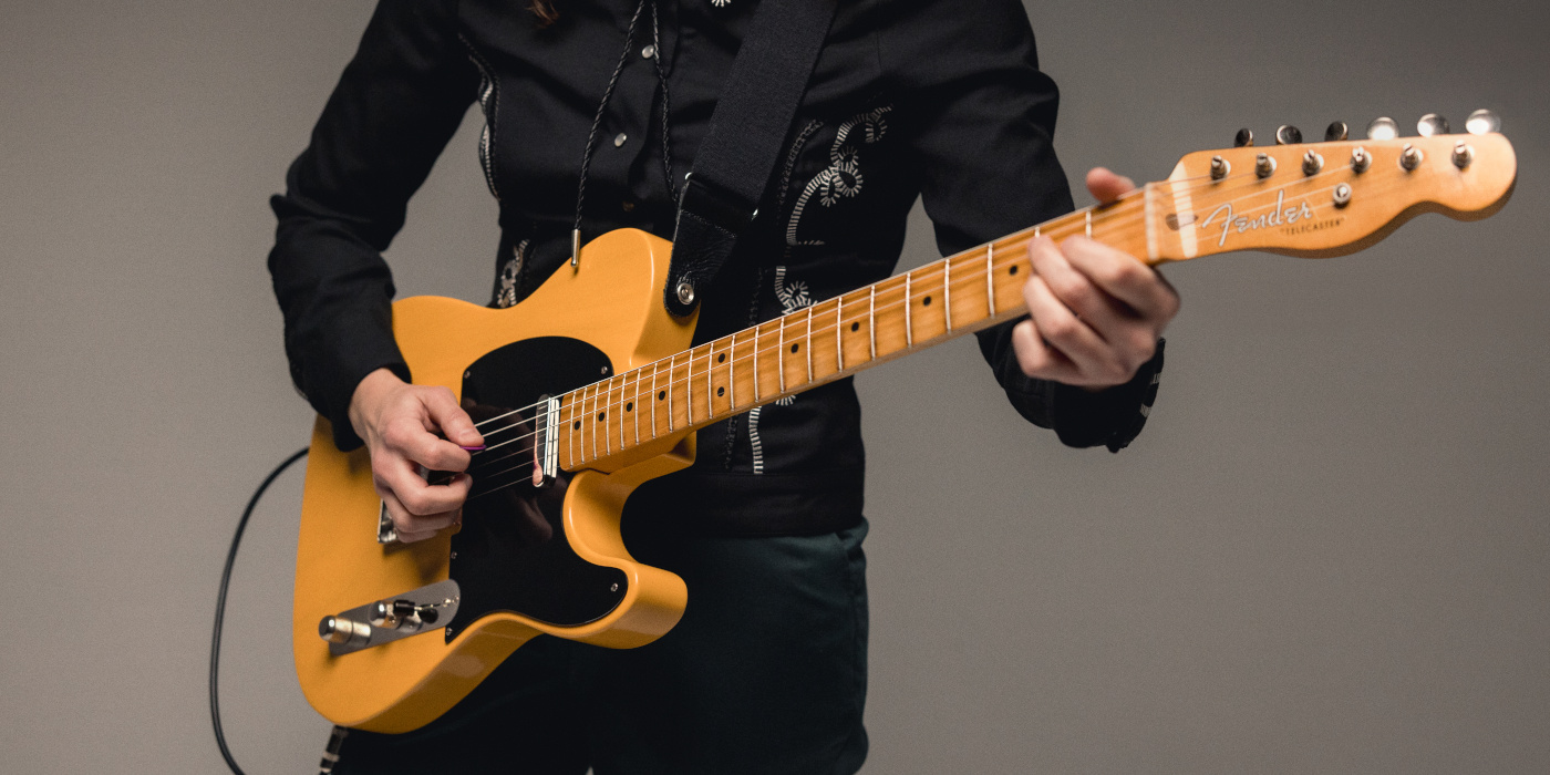 A person playing the Fender 75th Anniversary Vintera Road Worn 1951 Telecaster against a grey textured background
