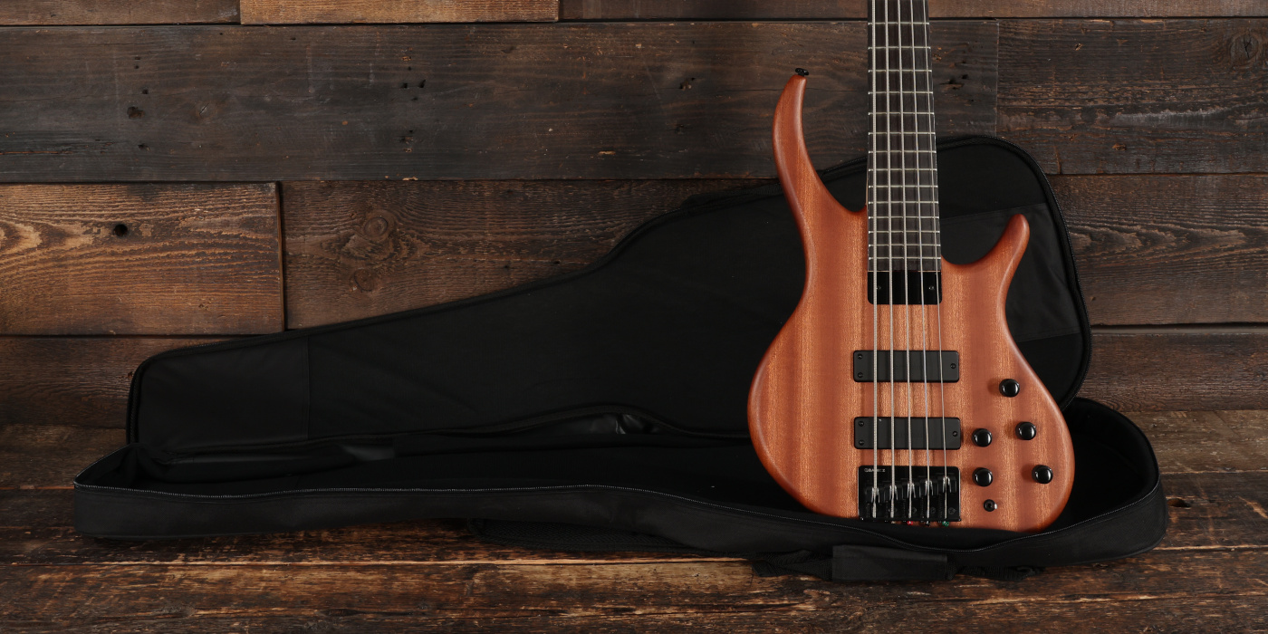 A photo of a natural finished Tobias Killer B 5-string bass with a black gig bag against a wooden background