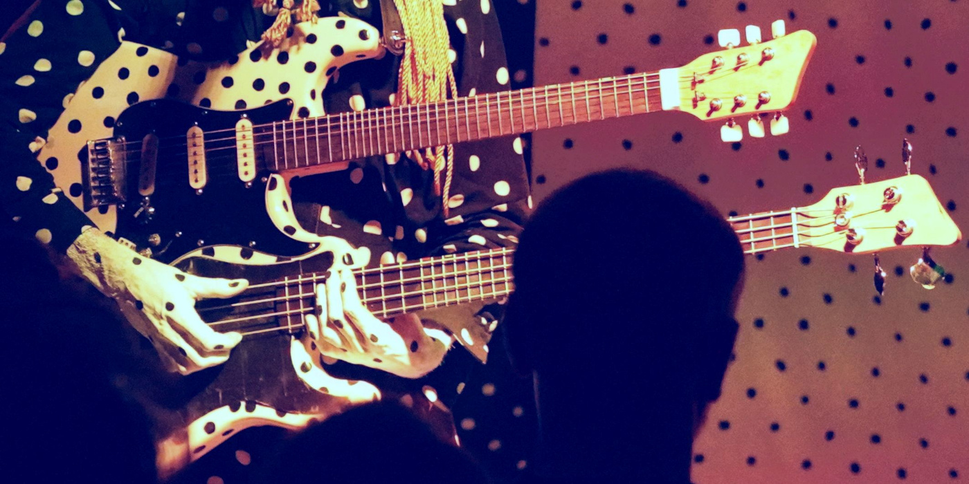 A close up photo of Angine de Poitrine playing a microtonal guitar with two necks on a stage