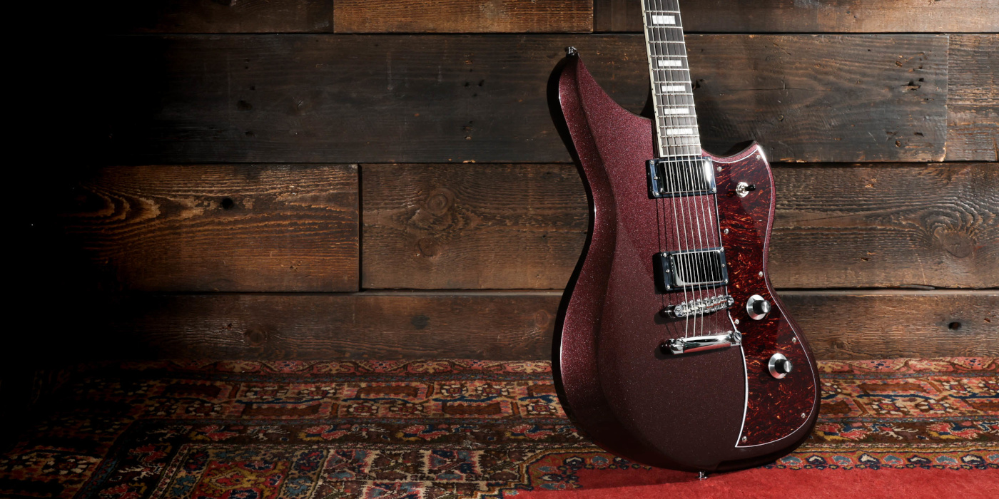 A Dunable Yeti DE electric guitar in oxblood on a fancy red carpet against a wooden background