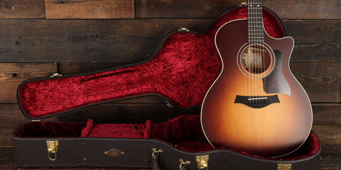 A studio photo of the Taylor The Last of Us Replica 314c acoustic guitar, sat in its included case against a wooden background