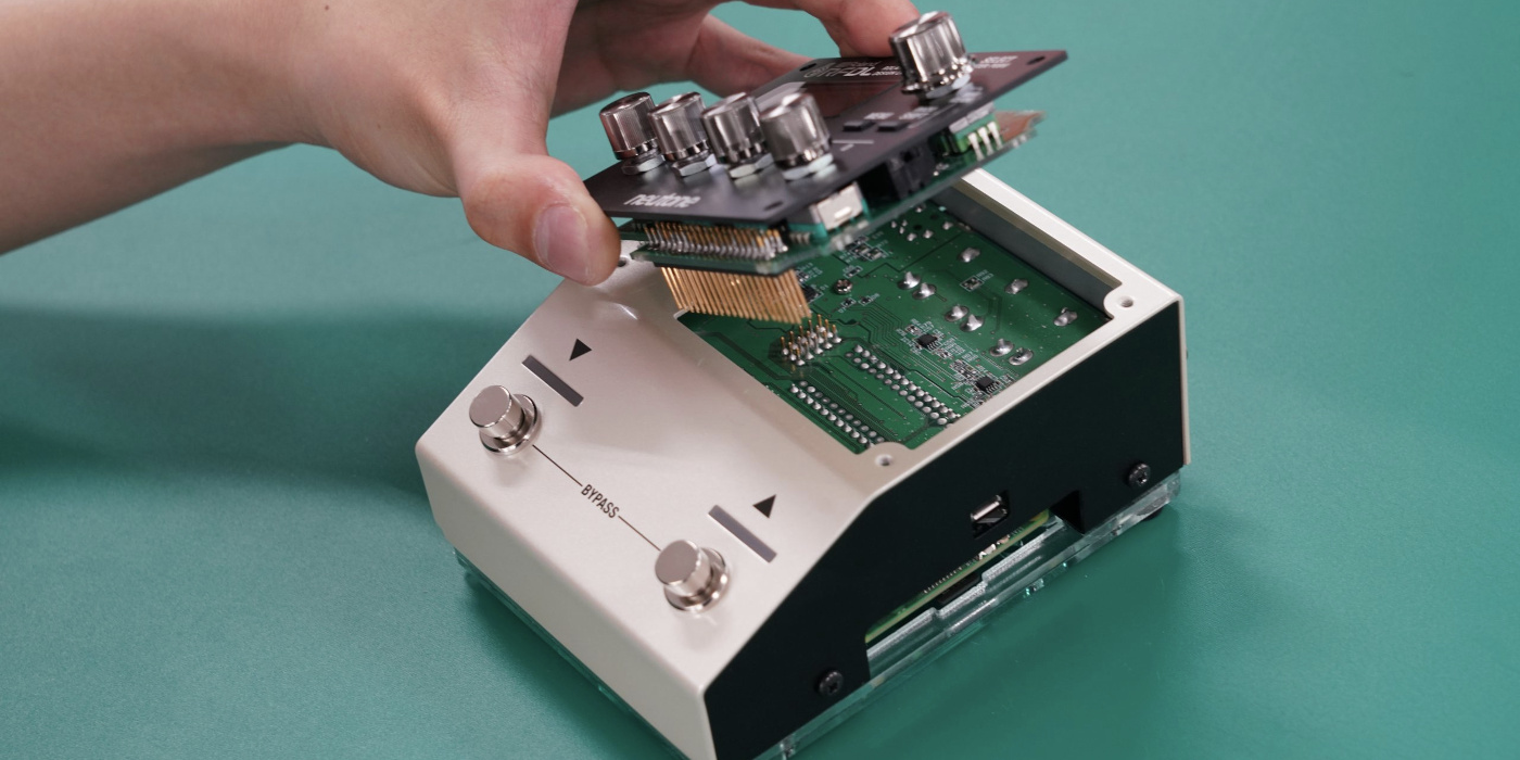 A photo of the Roland Project LYDIA Phase II pedal, with a hand lifting the screen to reveal the circuitry inside
