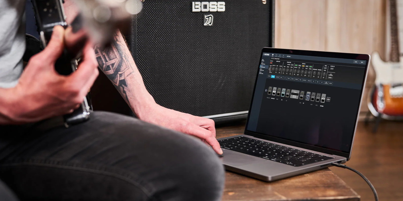 A photo of a man sitting with a guitar on his lap using the Boss Tone Studio app on his laptop in front of a Boss Katana combo amp