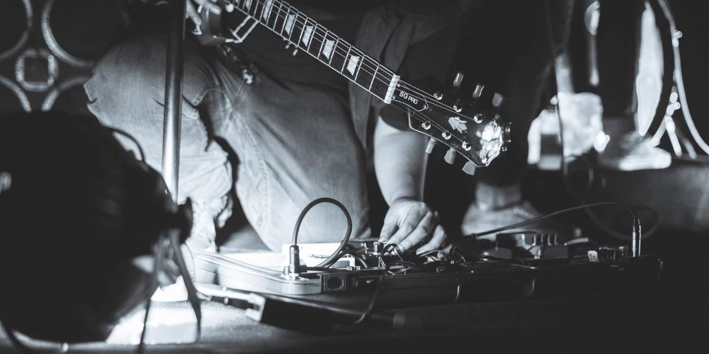 A gigging guitarist onstage tweaking settings on a pedal on their pedalboard