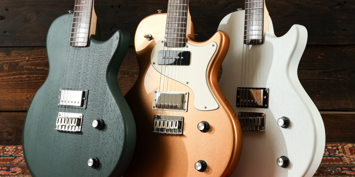 A photo of three PJD Carey Origin guitars lined up at an angle against a wooden background