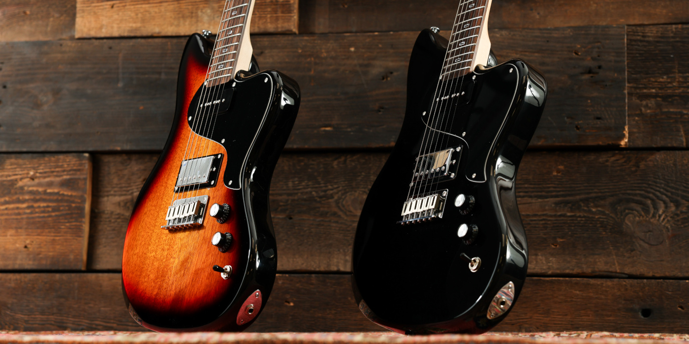 A photo of two PJD St. John Origin guitars in sunburst and black at an angle against a wooden background