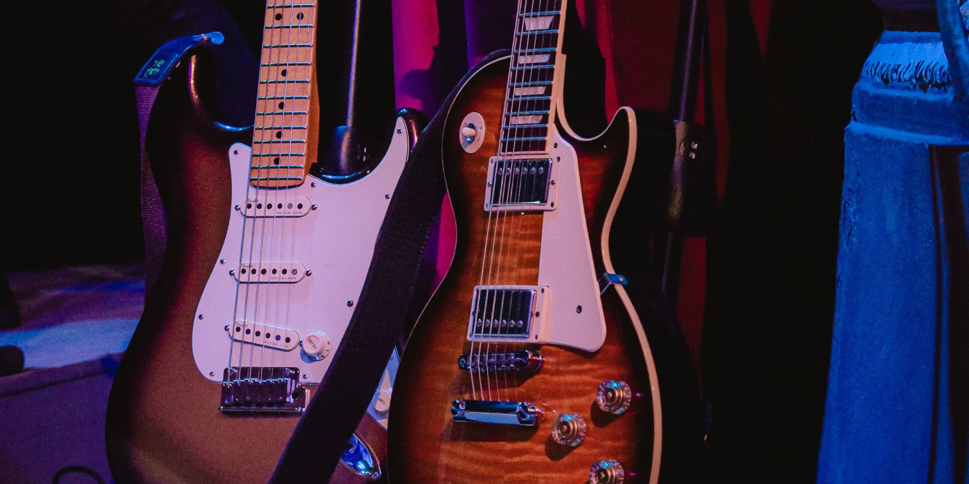 A Fender Stratocaster and Gibson Les Paul next to each other on a neon-lit stage