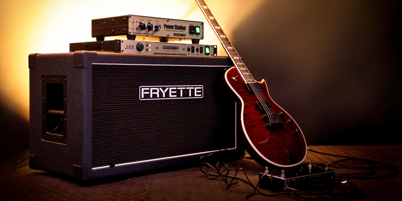 A Fryette Power Station PS-2A and LX II power amp stacked on top of a Fryette 2x12 cab with a red single-cut guitar leaning up against it