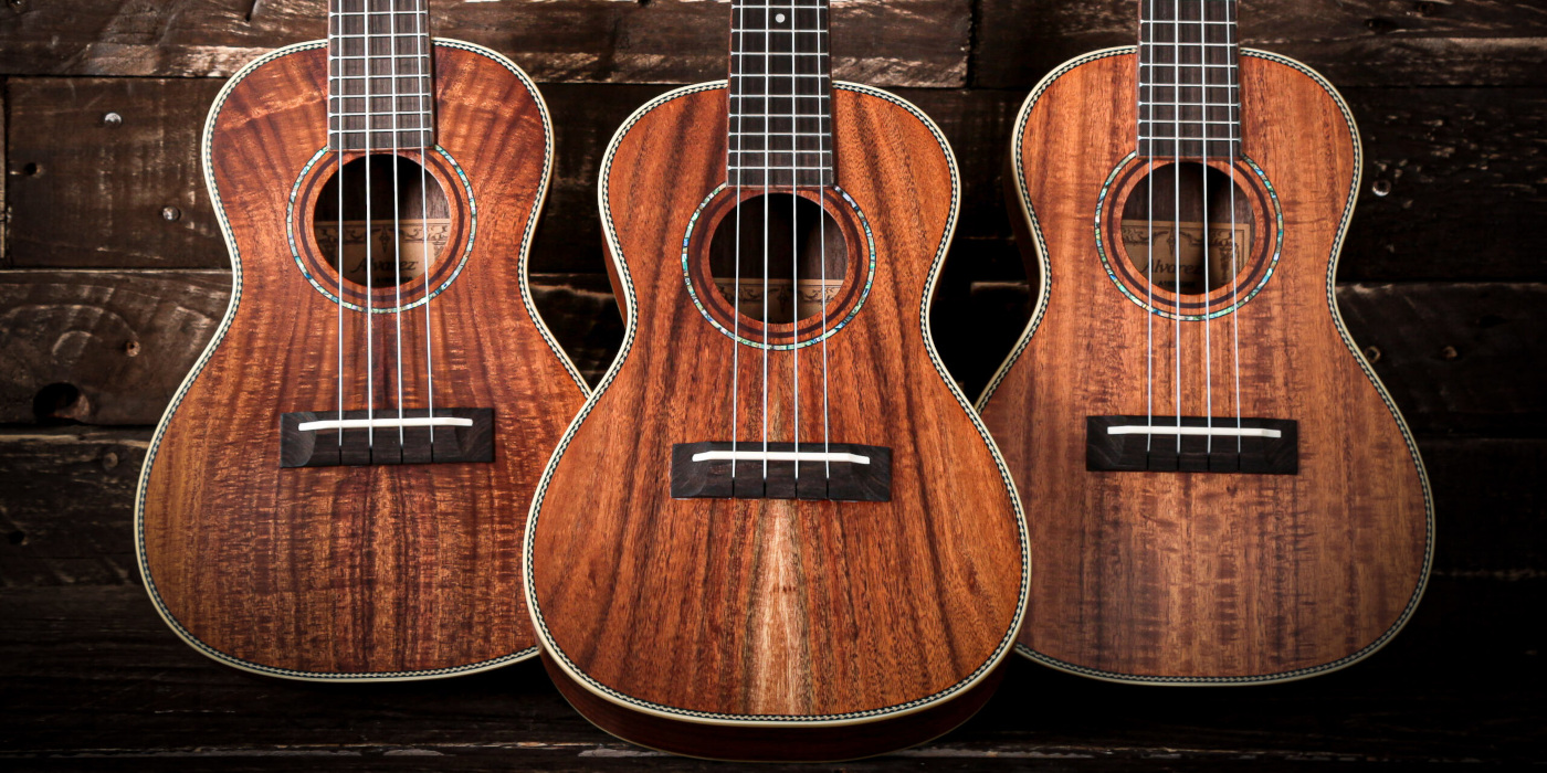 Three Alvarez natural wood ukulele models lined up against a dark wooden background