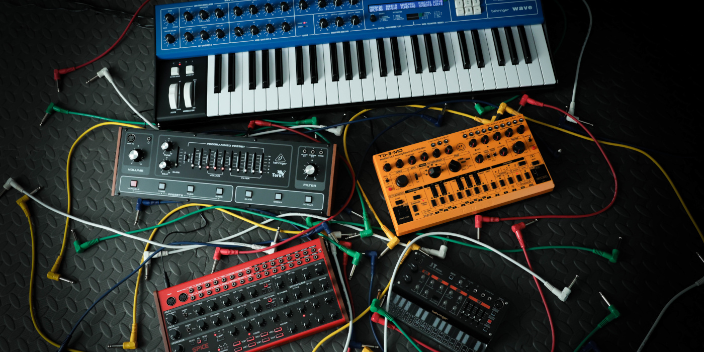 Behringer synthesizer models on a metal platform surrounded by patch cables