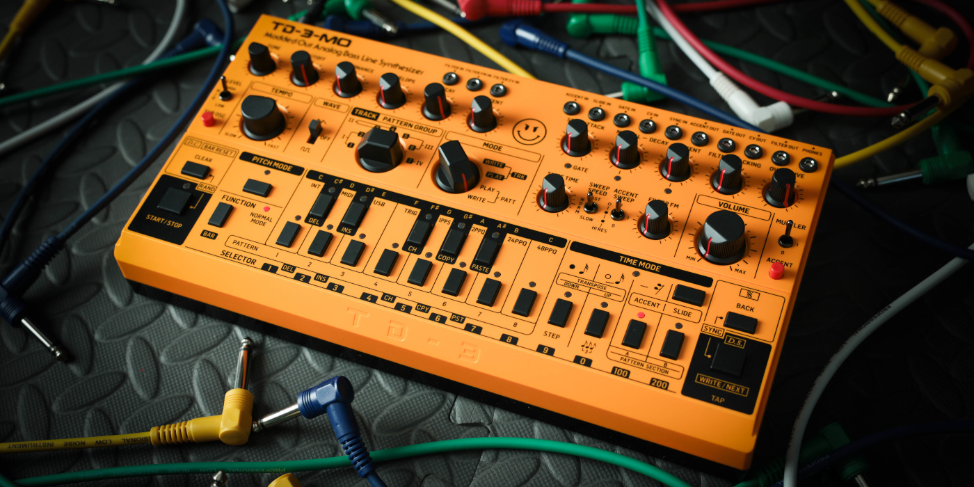 A photo of a Behringer-TD-3-MO bass synth at an angle from the front surrounded by multi-coloured patch cables