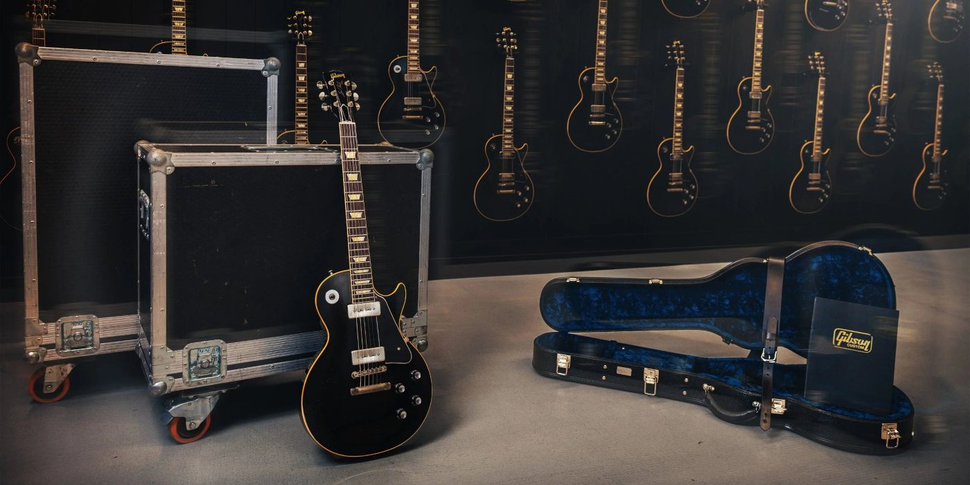 A photo of the Gibson Noel Gallagher signature Les Paul Standard electric guitar in a music studio next to its case with other guitars on a wall behind them