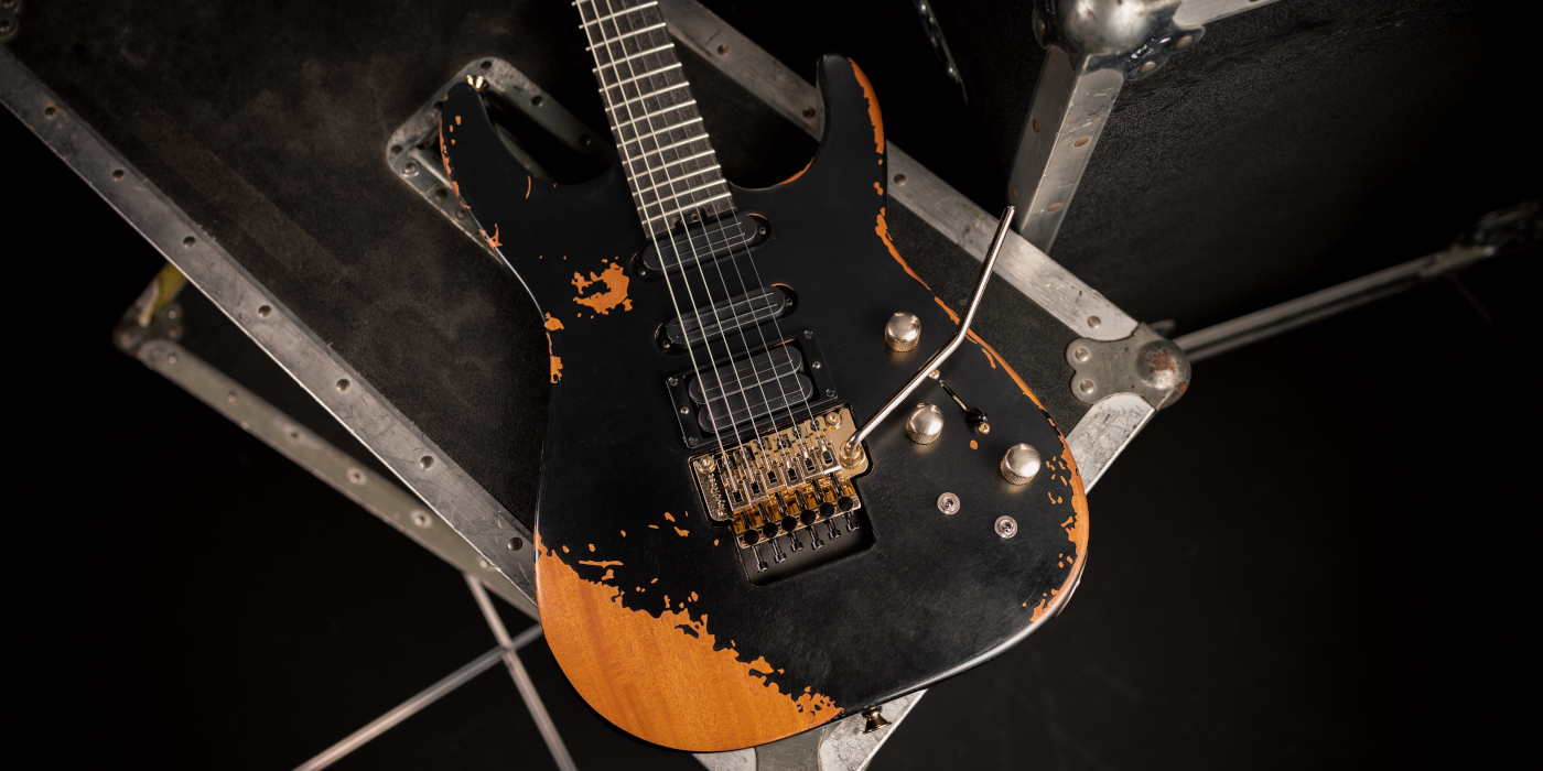 The Jackson Pro Series PC1-E Phil Collen signature guitar in Worn Black placed on a black tour case
