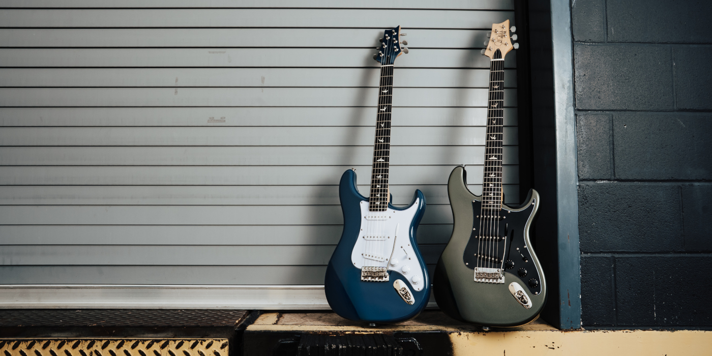 A photo of two PRS Silver Sky Defender guitars leaning up against a garage door