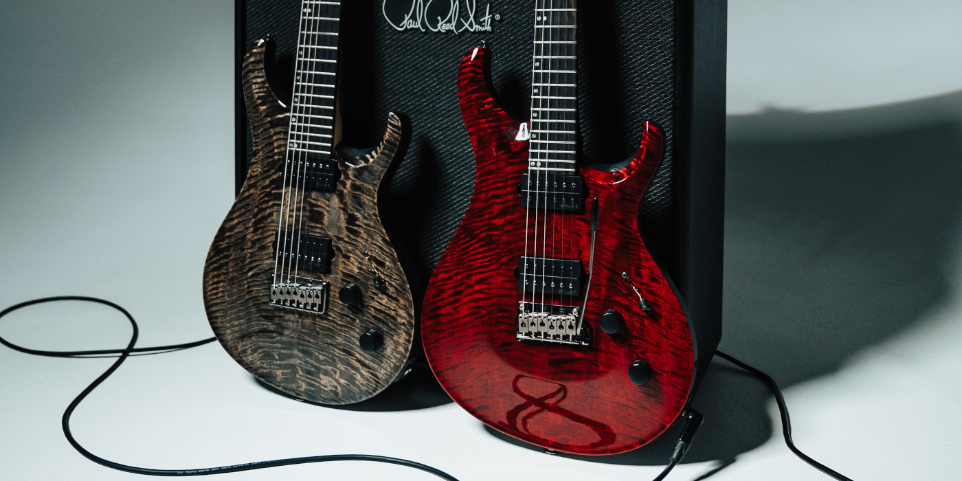 Two PRS Tekton guitars leaning up against a black amp