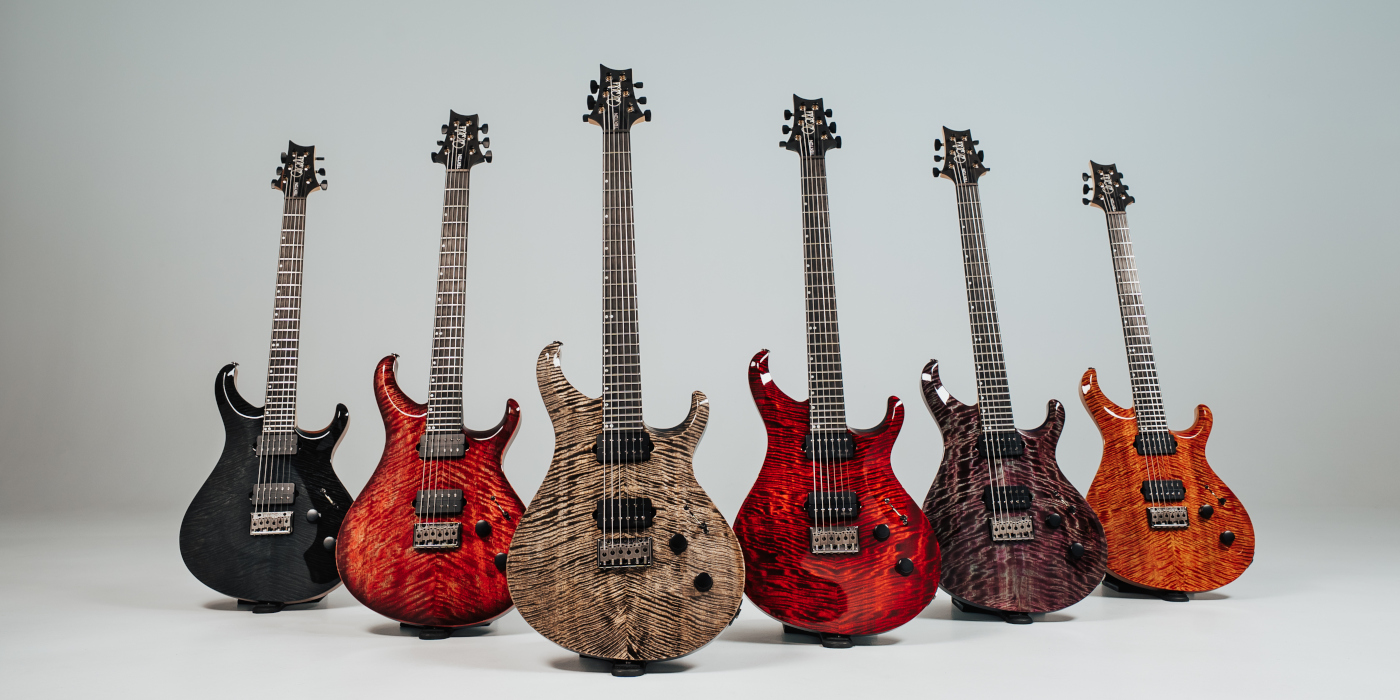 Six PRS Tekton hardtail electric guitars in various colours lined up against a textured grey background