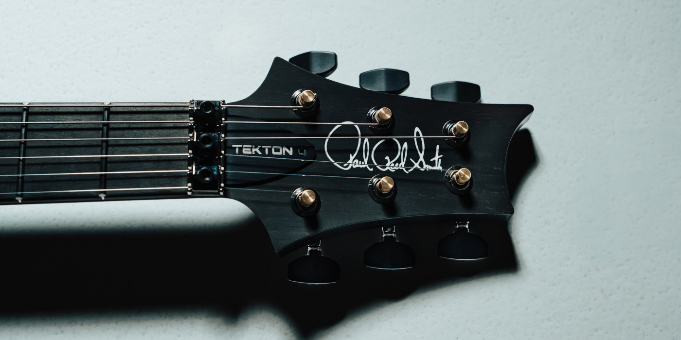 A black PRS Tekton guitar headstock on a light coloured background
