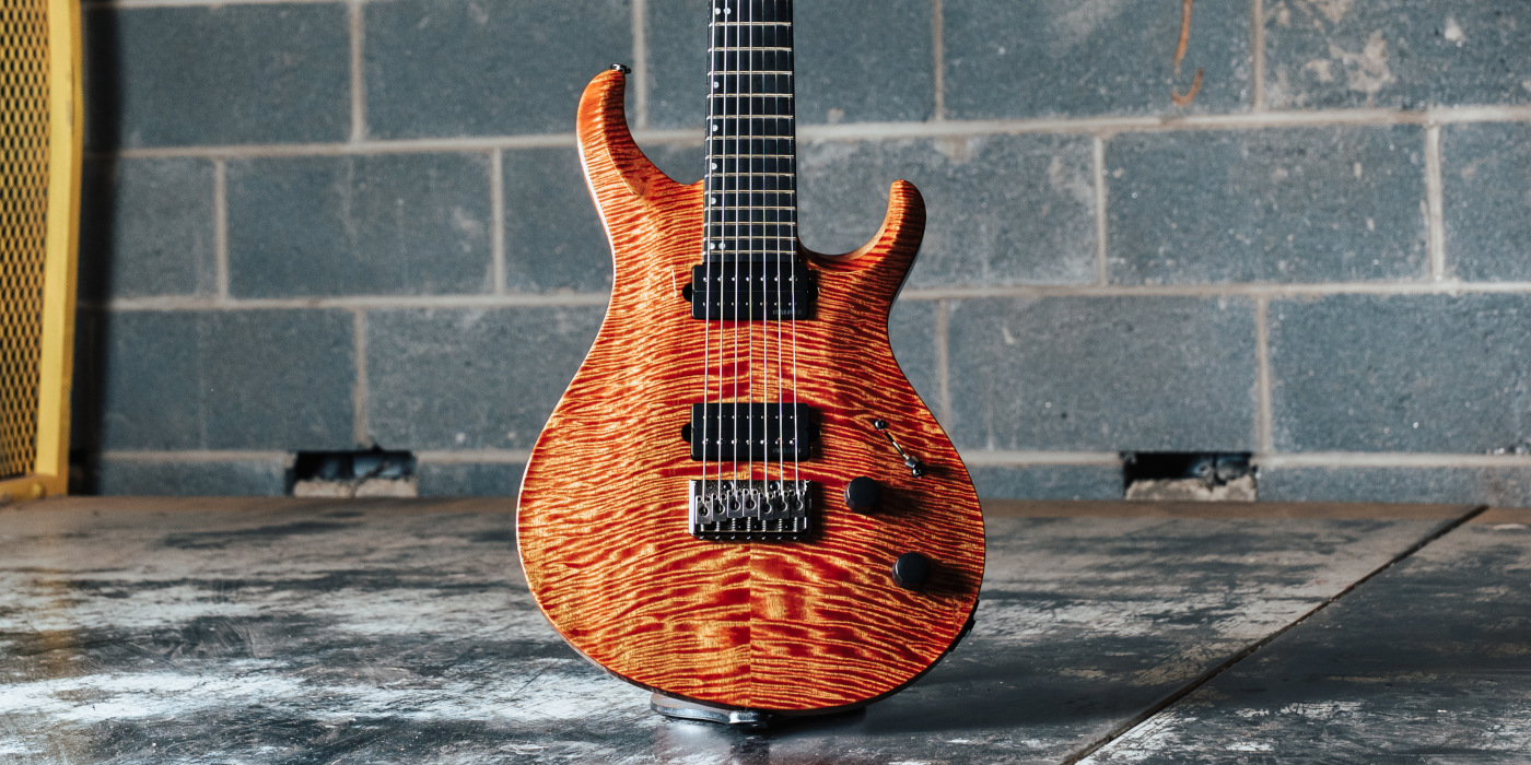 A PRS Tekton SVN 7-string electric guitar in Imperial Topaz against a grey brick wall