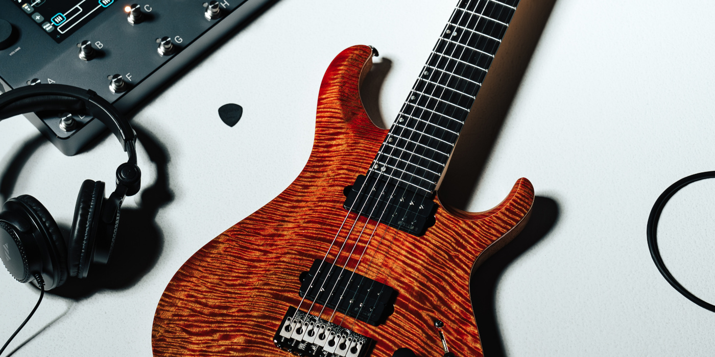 An orange PRS 7-string guitar on a grey floor next to a pair of headphones and a Neural DSP Quad Cortex
