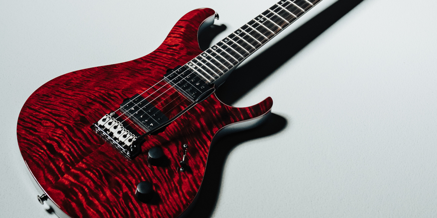 A PRS Tekton T guitar in red with a shadow on a grey floor